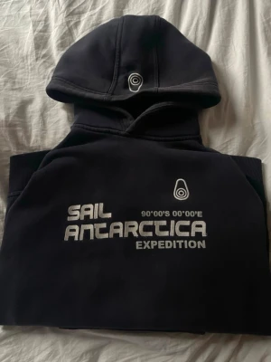 Mörkblå Sail Antarctica Expedition hoodie - Snygg mörkblå hoodie från Sail Antarctica Expedition med tryck på bröstet och patch på ärmen. 