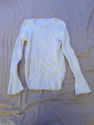 Vit ribbad stickad tröja med slits - Säljer en supermjuk vit stickad tröja med ribbad struktur och slits i sidan. Tröjan har lång ärm och lätt utsvängda ärmslut för en chill vibe. Perfekt till höst och vinter när du vill vara både varm och snygg.