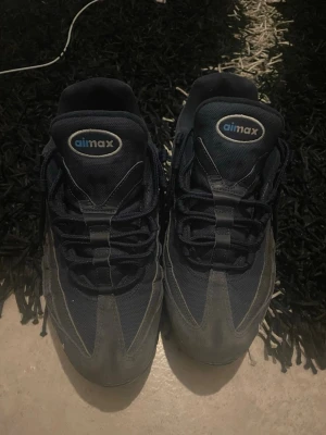 Nike Air Max 95 mörkblå sneakers - Nike Air Max 95 sneakers i mörkblått med klassisk vågig design och synliga luftbubblor i sulan. Ovandel i mesh och mocka med snörning och rund tå. Perfekta för dig som gillar streetwear och sportig stil.