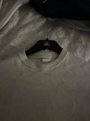 Beige stickad tröja från Zara - En stilren beige stickad tröja från Zara med rund halsringning och ribbade muddar vid hals, ärmslut och nederkant. Perfekt för lager-på-lager och enkel att matcha med olika outfits.