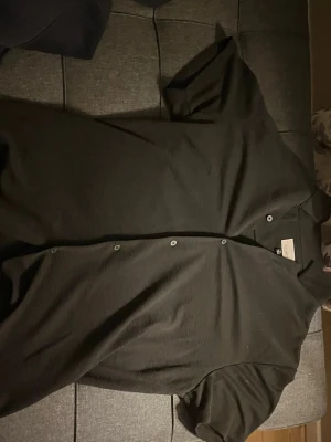 Svart kortärmad skjorta Civil Society - Säljer en svart kortärmad skjorta från Civil Society. Skjortan har klassisk krage, knappar framtill och är tillverkad i ett mjukt tyg som känns skönt mot huden. Perfekt för dig som gillar en clean och enkel stil.