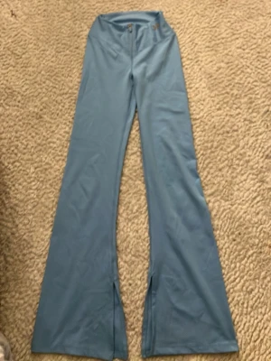 Blå leggings med slits framtill - Snygga blå leggings med utsvängda ben och slits framtill. De har hög midja och stängs med knapp och dragkedja. Perfekta för dig som vill ha en trendig och bekväm look.