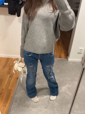 Blå slitna bootcut jeans - Säljer ett par blå bootcut jeans med slitningar och detaljerade rivna partier framtill. Jeansen har normal passform och klassisk femficksdesign. Perfekta för dig som gillar en avslappnad och trendig stil. jeansen är omsydda🩷