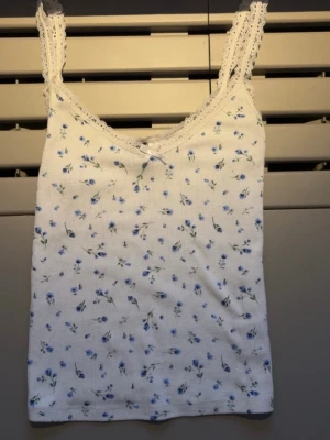 Sött linne med spets och blommor - Gulligt vitt linne med blå blommor, linnet har spets detalj och en liten rosett