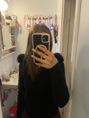 Svart hoodie med fluffig huva - Säljer en svart hoodie med dragkedja och stor, fluffig huva med fuskpäls runt kanten. Hoodien har långa ärmar och är gjord i ett mjukt material som känns skönt mot huden. Perfekt för dig som vill ha en mysig och stilren look. Den är helt ny då jag fick två i födelsedagspresent, bilderna när jag har den på mig är med den tröjan jag ska ha kvar. Den andra ligger kvar i plast och har prislappen kvar. Skriv vid frågor, pris går att diskutera.💕