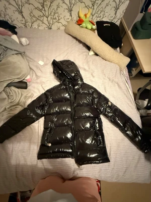 Svart glansig pufferjacka Moncler - Snygg svart pufferjacka från Moncler med glansig finish och huva. Jackan är i ett väldigt bra skick, knappast använd. Den är i storlek S men passar som en M också. 