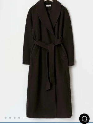 Mörkbrun lång kappa med bälte - Säljer en lång och oversized mörkbrun kappa med bred krage och knytskärp i midjan. Jackan har stora fickor och en stilren look som passar perfekt till höst och vinter. Materialet känns mjukt och värmande, och modellen har långa ärmar.