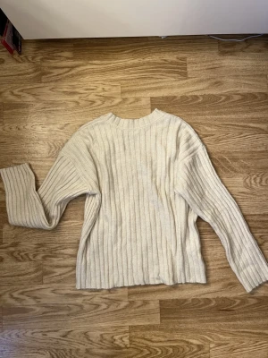 Ribbad beige stickad tröja NA-KD XS - Ribbad beige stickad tröja från NA-KD i storlek XS. Tröjan har v-ringning bak, lång ärm och en loose fit. Perfekt till lager på lager och enkel att styla med jeans eller kjol. 