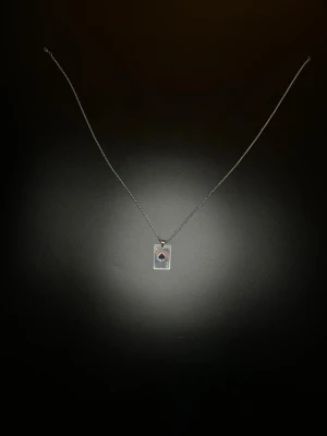 Halsband med ess i spader-hänge - Snyggt halsband i silverfärg med ett rektangulärt hänge format som ett spelkort, ess i spader. Kedjan är stilren, och hänget har tydliga detaljer med svart spader-symbol. Perfekt för dig som gillar kortspel eller vill ha en unik accessoar.