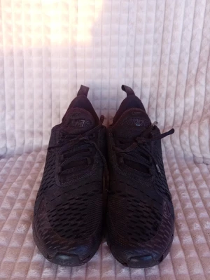 Nike Air Max 270 helsvarta sneakers - Säljer ett par helsvarta Nike Air Max 270 sneakers med mesh-ovandel och synlig Air-enhet i hälen. Skorna har snörning, rund tå och platt sula. Perfekta för dig som gillar sportig stil och vill ha bekväma skor till vardags.