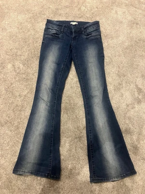 Mörkblå bootcut jeans med utsvängda ben - Snygga mörkblå bootcut jeans med utsvängda ben och klassisk femficksdesign. Jeansen har en tvättad look med ljusare partier längs benen och är tillverkade i ett mjukt denimtyg. Perfekta för dig som gillar retrovibbar och vill ha en bekväm passform.