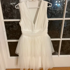Vit kortklänning med v-ringning - Supersöt vit kortklänning med djup v-ringning och lager på lager av tunt, skirt tyg. Klänningen är ärmlös och har markerad midja som ger en snygg siluett. Perfekt för studenten. Storleken är M men klänningen har blivit insydd i midjan så att den passar s. Köpt från Gina Tricot 