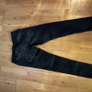 Svarta skinny jeans - Svarta skinny jeans med lätt tvättad look och klassiska fem fickor. Jeansen har smal passform och normal midja, perfekta för en stilren och modern outfit. Materialet är stretchigt jeans för extra komfort.