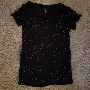 Svart prickig kortklänning H&M - Svart kortklänning från H&M med små vita prickar över hela tyget. Klänningen har rund halsringning och korta ärmar, perfekt för en avslappnad och stilren look. Tillverkad i mjukt material som känns skönt mot huden.