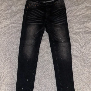 Svarta  jeans från Purple Brand - Svarta jeans från Purple Brand med skön fit och coola slitningar samt vita färgstänk för en edgy look. Jeansen har klassisk femficksdesign, knappgylf och diskreta detaljer. Perfekta för dig som gillar streetwear och vill sticka ut.