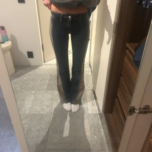 Bootcut jeans med kontrasttvätt - Säljer ett par mörkblå bootcut jeans från Weekday med cool kontrasttvätt i beige längs sidorna. Jeansen har låg midja, klassisk femficksdesign och är tillverkade i jeansmaterial. Perfekta för dig som vill sticka ut med en unik look.