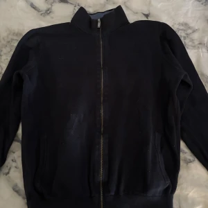 Svart kofta från Massimo Dutti - Svart kofta från Massimo Dutti med hel dragkedja och ståkrage. Tröjan är tillverkad i mjuk bomull och har ribbade muddar vid ärmslut och nederkant. Perfekt för lager-på-lager och chill dagar. Snygg, enkel och stilren design.