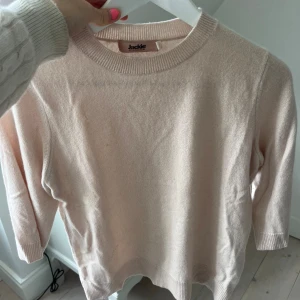 Ljusrosa stickad tröja från Jackie - Snygg ljusrosa stickad tröja från Jackie med rund hals och ribbade muddar. Modellen har trekvartsärm och är perfekt för dig som gillar en enkel och stilren look. Mjuk och skön kvalitet som passar till många olika outfits.