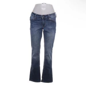 Blå bootcut jeans från Guess - Snygga blå jeans från Guess med klassisk bootcut-passform. Jeansen har fem fickor, orangea kontrastsömmar och en lätt tvättad look. Tillverkade i jeansmaterial som ger en skön känsla och stilren vibe.