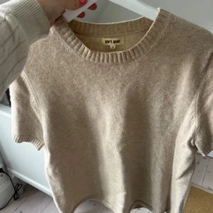 Beige stickad tröja Soft Goat - Superskön beige stickad tröja från Soft Goat i storlek S. Tröjan har korta ärmar och rund hals med ribbad kant. Perfekt för dig som gillar mjuka material och enkel stil. Passar till jeans eller kjol för en chill look.