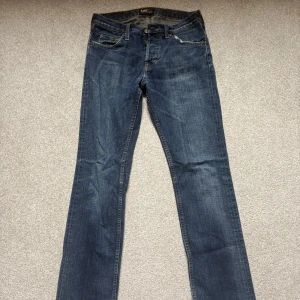Mörkblå Lee jeans straight fit - Snygga mörkblå jeans från Lee med klassisk femficksdesign och raka ben. Jeansen har slitna detaljer vid bensluten och subtila slitningar framtill. Tillverkade i robust denim med kontrastsömmar och Lee-logga på bakfickan.