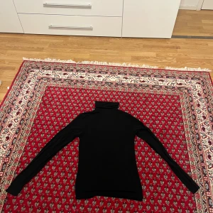 Svart polotröja från Amisu - Svart polotröja från Amisu i storlek M. Tröjan är långärmad och har en klassisk polokrage. Tillverkad i mjuk och stretchig viskosblandning med 5% elastan för en tight och bekväm passform. Perfekt att styla med jeans eller kjol.