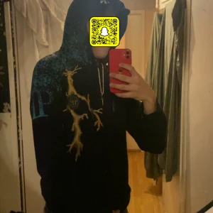 Philipp Plein hoodie med dödskalle - Säljer en svart hoodie från Philipp Plein med huva och snörning. Framsidan har ett blixtliknande mönster i gult och blått, samt logga på bröstet. Baksidan har en stor gul dödskalle och texten 'PLEIN' i vitt. Grym streetstyle vibe! 