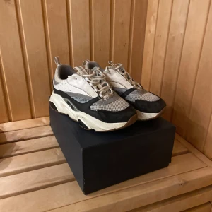 Chunky sneakers från Dior, grå/vit - Säljer ett par chunky sneakers från Dior i grått, vitt och svart med meshdetaljer och kraftig sula. Skorna har snörning och coola kontraster mellan material och färger. Perfekta för dig som gillar statement sneakers och exklusiv streetstyle.