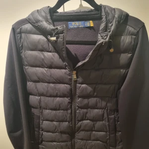 Svart jacka från Polo Ralph Lauren - Svart jacka från Polo Ralph Lauren med quiltad framsida, huva och dragkedja. Jackan har släta ärmar och baksida i mjukt material, samt justerbar dragsko i huvan. Perfekt för lite kyliga dagar och snygg till streetwear. Fast pris. Inga byten. 
