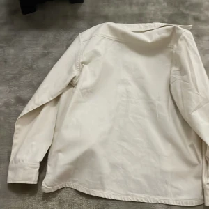 Vit overshirt från Name It - Snygg vit overshirt från Name It med klassisk krage och två stora bröstfickor med lock. Skjortan har långa ärmar och knappar framtill. Perfekt att bära som lager över en t-shirt för en clean och chill look.