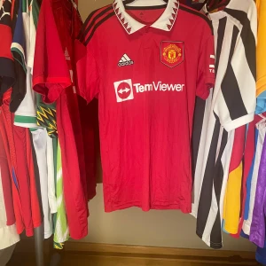 Manchester United Adidas hemmatröja 2022/23 XS Äkta Fotbollströja - Röd Manchester United fotbollströja från Adidas från 2022/23 säsongen med vit krage och svarta detaljer på axlarna. Broderad klubbmärke på bröstet, nopprig i kragen  men annars i bra skick. Äkta