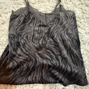 Zebramönstrad linnetopp från Hunkemöller - Säljer en snygg zebramönstrad linnetopp från Hunkemöller i grå och svarta toner. Toppen har tunna axelband, spetsdetaljer vid urringningen och en loose passform. den är storlek M men passar S och har inga defekter❣️
