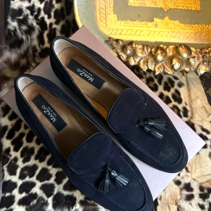 Marzio navy blue loafers i mocka med tofsar - Mörkblåa loafers i mocka från Marzio på Nybrogatan med tofsar framtill. 100% skinnsko med låg klack, samt påkostad gummisula från Vibram. Tillverkade i Italien. Mycket bra skick förutom skavet på vänster sko (synligt på bild)