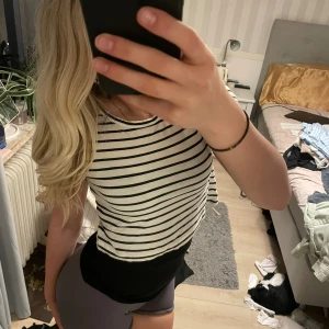 Randig topp från H&M - Säljer en vit och svart randig topp från H&M. Modellen har rund hals och croppad passform, perfekt till jeans eller shorts. Materialet är mjuk och känns skönt mot huden. 