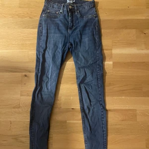 Blå skinny jeans från 157 - Snygga blå skinny jeans från 157 med klassisk femficksdesign och gul kontrastsöm. Jeansen har hög midja och är tillverkade i stretchigt denim för en tight passform. Perfekta att matcha med en hoodie eller t-shirt för en avslappnad look.