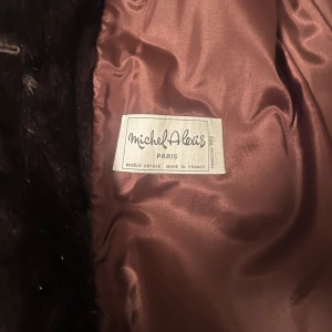 Mörkbrun pälsjacka från Michel Alexis - Säljer en lång, lyxig pälsjacka från Michel Alexis Paris i mörkbrun färg. Jackan har en klassisk krage och är helfodrad med glansigt tyg på insidan. Perfekt för dig som vill sticka ut med en elegant och tidlös look. Vintage! 