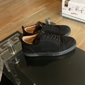 Svarta sneakers från Christian Louboutin - Säljer ett par svarta sneakers från Christian Louboutin med matt finish och snygga svarta snören. Insidan är beige och yttersulan har den klassiska röda färgen med Louboutin-logga. Skorna har rund tå och platt sula, tillverkade i mocka för en lyxig känsla.