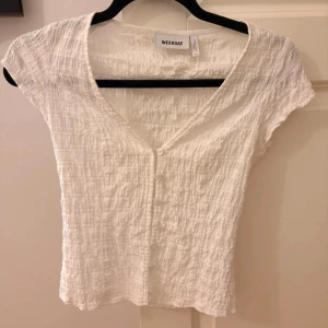 Vit blus från Weekday med knappar - Säljer en söt vit blus från Weekday i storlek 34. Toppen har korta ärmar, v-ringning och knappar framtill. 💞slut såld