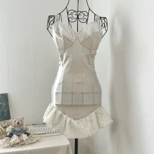 Vit satin klänning med spetsvolang - Supersöt vit kortklänning med figurnära passform och en bred spetsvolang längst ner som ger en romantisk vibe. Passar byst 85-90cm, underbyst 70-75cm. Dockan har storlek 34. Färgen är snarare benvit/ljus beige.