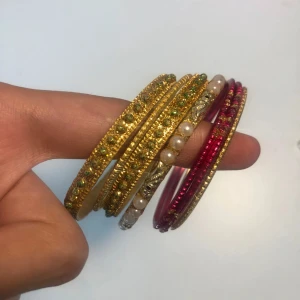 Färgglada armband med pärlor och stenar - Säljer ett set med flera smala armband i guld, gult och rosa. Några armband har glittriga stenar, andra är dekorerade med vita pärlor. Perfekt för dig som gillar att mixa och matcha färger och detaljer.