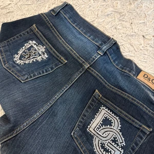 Dolce & Gabbana jeans - Mörkblå jeans från Dolce & Gabbana med snygga broderade detaljer och logga på bakfickan. Några av stenarna har ramlat av då de är vintage men är i mycket bra skick. Står att den är storlek 34, se mått