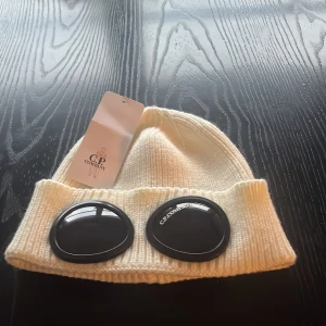 Vit C.P. Company goggle mössa - Säljer nu min oanvända C.P company vintermössa, väldigt bekväm och varm nu till vintern. Aldrig använd endast testad och allt som syns på bilden fås med. Passar väldigt bra på alla huvudformer och är väldigt bekväm mössa. Vid frågor är det bara att komma privat😃