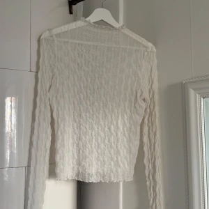 Vit långärmad meshblus från Gina Tricot - Säljer en vit långärmad meshblus från Gina Tricot i storlek M. Blusen har ett vågigt, transparent tyg med lätt struktur och volangkant vid halsen