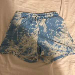 Blå tie-dye shorts med snörning - Snygga blå och vita tie-dye shorts med elastisk midja och snörning framtill. Mjukt material som känns chill och har fickor på sidorna. Perfekta för varma dagar och har en loose passform som ger skön vibe.