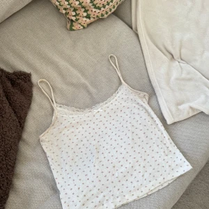 Blommig linnetopp från John Galt - Supersöt linnetopp från John Galt i ljusbeige med små rosa blommor och gröna detaljer. Spaghettiband, spetskant vid halsen och en liten rosett framtill