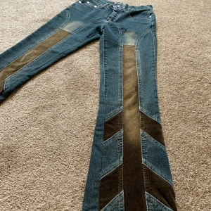 Blå jeans med bruna detaljer Blue Qier - Unika lågmidjade utsvängda blå jeans från Blue Qier i storlek S med bruna manchesterpaneler längs benen och bakfickorna. Snyggt mönstrade detaljer framtill och bak, klassisk femficksmodell och raka ben. Materialmix av denim och manchester för en cool look.