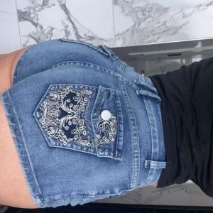 Blå jeansshorts med broderad ficka - Snygga blå jeansshorts med en broderad bakficka och knappdetalj. Klassisk femficksmodell med bälteshällor och normal passform. Perfekta för varma dagar och en avslappnad stil.