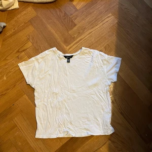 Vit basic t-shirt från H&M - En klassisk vit t-shirt från H&M i mjuk bomull. T-shirten har korta ärmar, rund halsringning och en avslappnad passform. Perfekt till jeans eller shorts för en enkel och clean look.