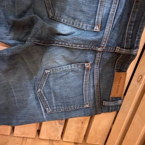 Blå Acne Jeans straight fit - Säljer ett par klassiska blå jeans från Acne Jeans med snygg tvätt och raka ben. Jeansen har fem fickor, orangea sömmar och läderpatch med logga bak i midjan. Perfekta för dig som gillar stilrena och tidlösa jeans.