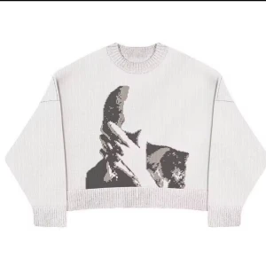 Vit stickad tröja med Frank ocean - Vit stickad tröja med oversized passform och rund hals. Framsidan har ett stort grafiskt motiv i svart och grått som föreställer en hand och en katt. Tröjan har långa ärmar och ribbade muddar vid ärmslut och nederkant. Perfekt för dig som gillar unika prints.